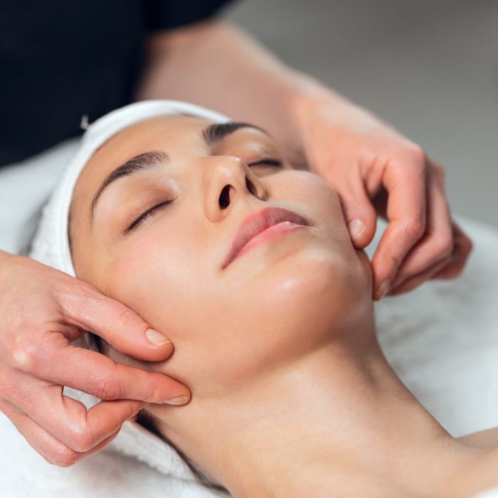 Shot of cosmetologist making face massage for rejuvenation to woman while lying on a stretcher in the spa center.